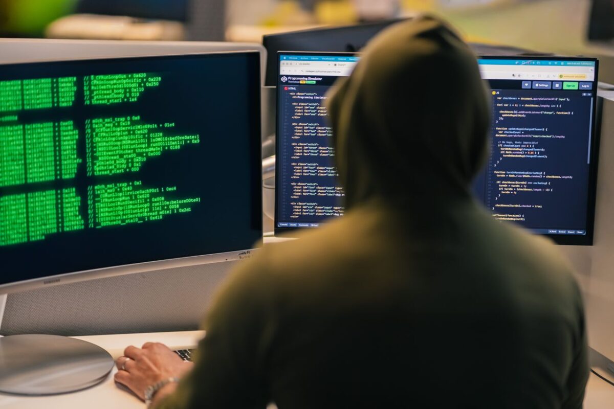 Respublicanova A person in a hoodie coding on dual monitors, depicting cybersecurity and hacking themes.