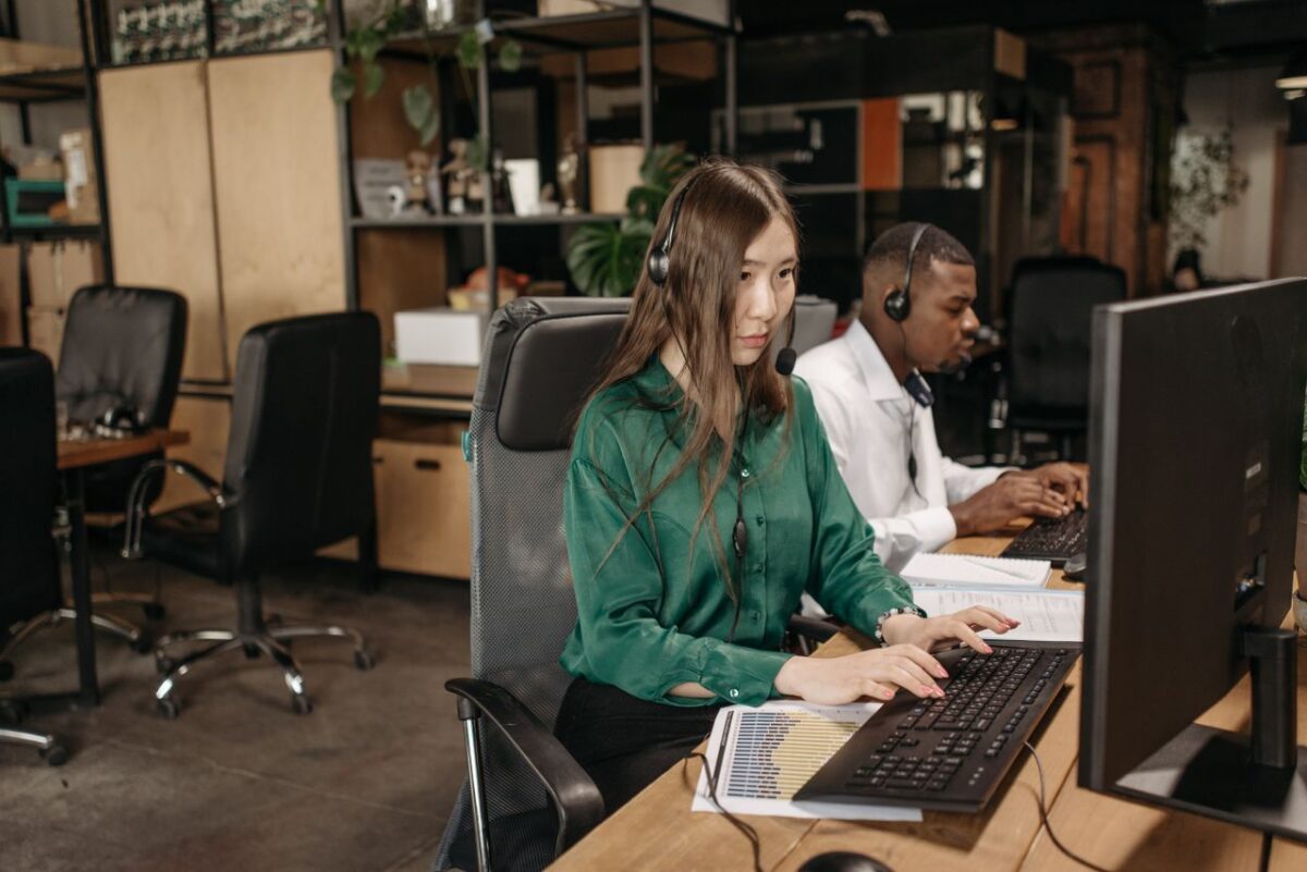 Offres Colleagues using computers and headsets in a modern office setting emphasizing teamwork and productivity.