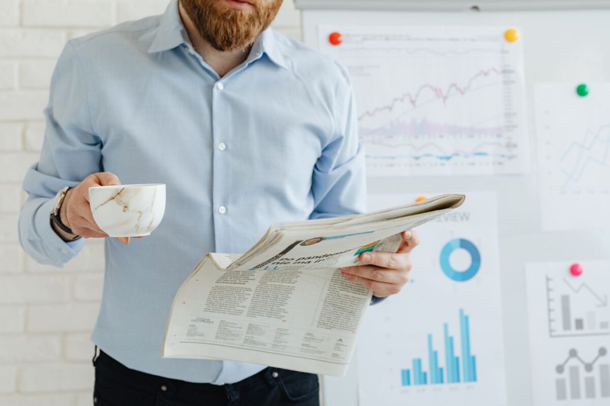 Offres Business person holding coffee and newspaper in office with charts.